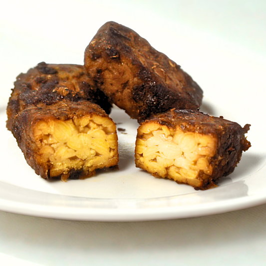 Upclose of three pieces of fried tempeh on a white plate with a white background