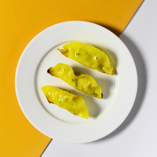 Three chicken dumplings on a white plate with a yellow background