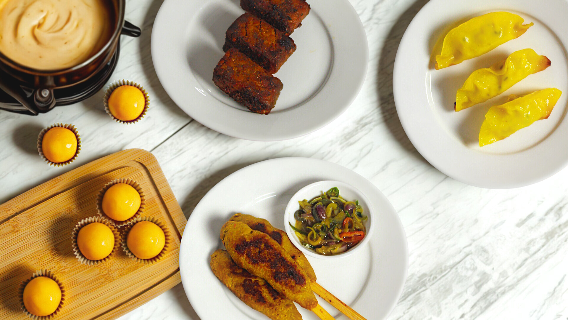 Assorted food items including skewers, dumplings, and pastries on a white surface.
