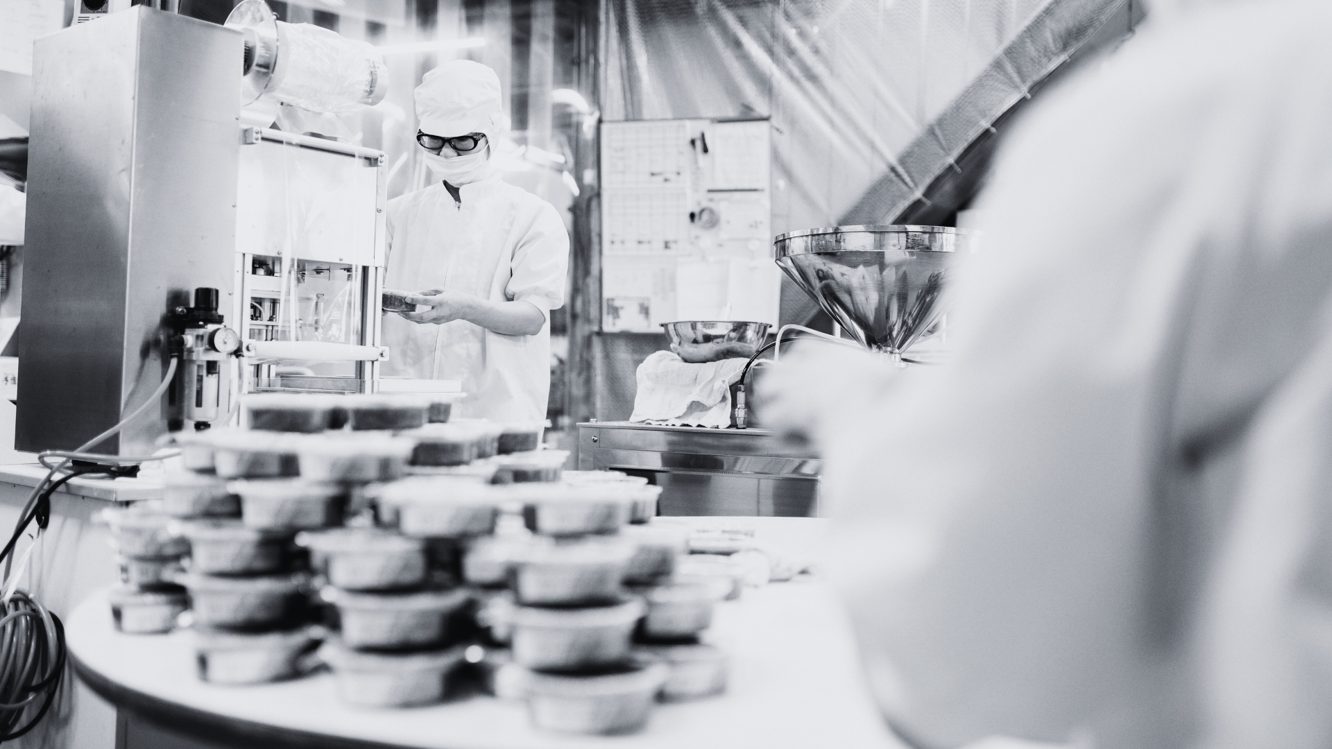 Person in a factory setting with machinery and products on a table.