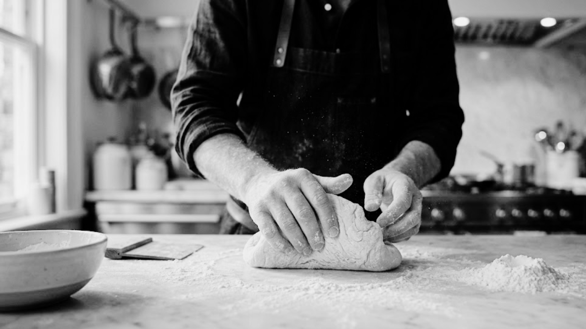 Person kneading dough on a wooden surface in a kitchen.